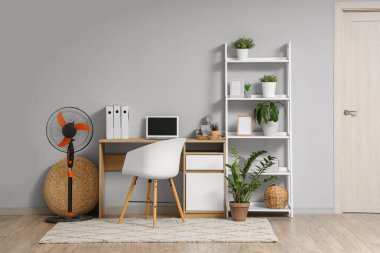 İş yerindeki masada yer elektrikli vantilatörü ve dizüstü bilgisayar.