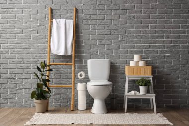 Tuvalet klozeti, merdiveni ve tuvalet kağıdı ile gri tuğla duvarın yanında raf ünitesi olan bir tuvalet.