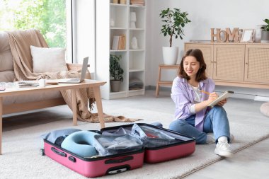 Evde bavulunu toplarken yazan genç bir kadın. Seyahat kavramı