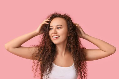 Pembe arka planda sağlıklı nemlendirilmiş cilde sahip mutlu genç Afro-Amerikan kadın.