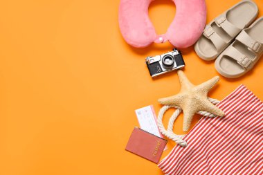 Travel pillow, photo camera and beach accessories on orange background clipart