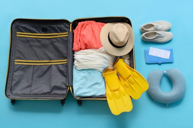 Seyahat yastığı, içinde giysiler ve mavi arka planda plaj aksesuarları olan valiz.