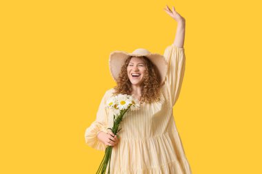 Sarı arka planda bir buket papatya çiçeğiyle mutlu genç kadın.