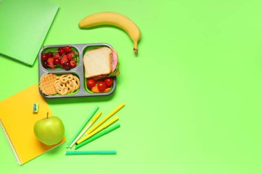 Okul malzemeleri, içinde böğürtlen ve yeşil arka planda sandviç olan beslenme çantası. Üst görünüm