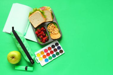 Okul malzemeleri, içinde böğürtlen ve yeşil arka planda sandviçler olan beslenme çantası. Üst görünüm
