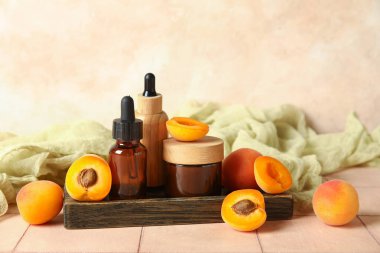 Kozmetik yağ şişeleri ve bej döşeme masasında taze kayısılarla dolu bir kavanoz krema.