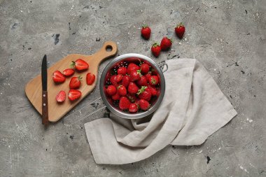 Kolander ve ahşap tahta üzerinde gri arkaplanda taze çilekler