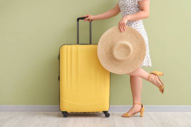 Yeşil arka planda hasır şapkalı ve bavullu genç bir kadın.