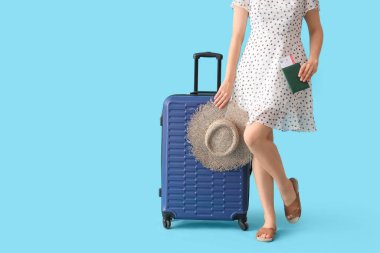 Bavulu, şapkası, pasaportu ve mavi arka planda bileti olan genç bir kadın.