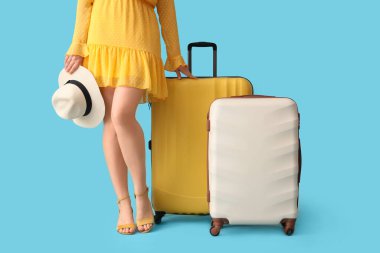 Mavi arka planda bavulları ve şapkası olan genç bir kadın.