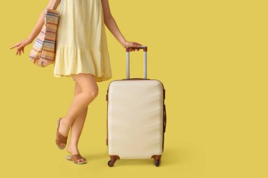 Sarı arka planda bavulu ve çantası olan genç bir kadın.
