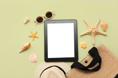 Yeşil arka planda güneş gözlüklü tablet ve plaj aksesuarları. Üst görünüm