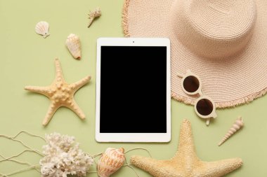 Tablet ve plaj aksesuarları, yeşil arka planda şapka ve deniz yıldızı. Üst görünüm