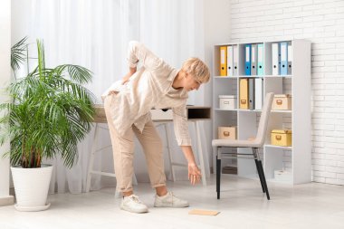 Olgun bir kadın evrak topluyor ve ofiste sırt ağrısı çekiyor.