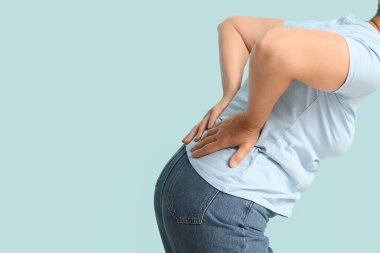 Evde mavi arka planda sırt ağrısı çeken olgun bir kadın.