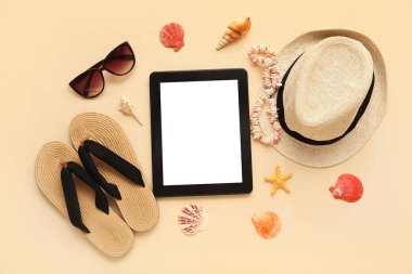 Tablet ve plaj aksesuarları, parmak arası terlik ve bej arka planda şapka. Üst görünüm