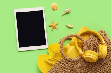 Çantalı tablet ve plaj aksesuarları ve yeşil arka planda deniz kabukları. Üst görünüm