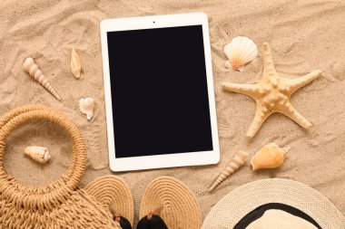 Tablet ve plaj aksesuarları, parmak arası terlikler ve kumdaki deniz yıldızları. Üst görünüm