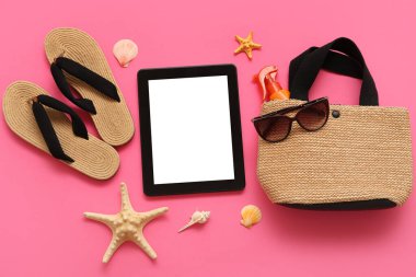 Tablet ve plaj aksesuarları, parmak arası terlik ve pembe arka planda güneş gözlüğü. Üst görünüm