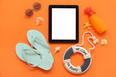 Tablet ve plaj aksesuarları, parmak arası terlik ve turuncu arka planda güneş kremi. Üst görünüm