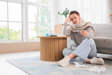 Evde termometresi olan, fularlı hasta genç bir kadın.