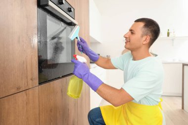 Mutfakta sprey şişesi ve cam temizleme fırını olan genç bir adam.