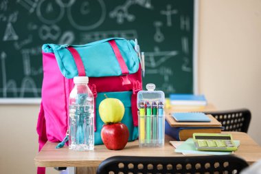 Sınıftaki masada su şişesi ve sırt çantalı elmalar.