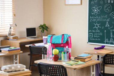 Sınıftaki masada su şişesi ve sırt çantalı elmalar.