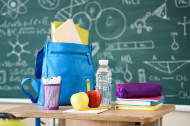 Okul kırtasiyeli elmalar, su şişesi ve sırt çantası sınıfta, yakın plan.