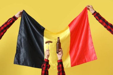 Alman bayrağı taşıyan eller, sarı arka planda sosis ve bira şişesi