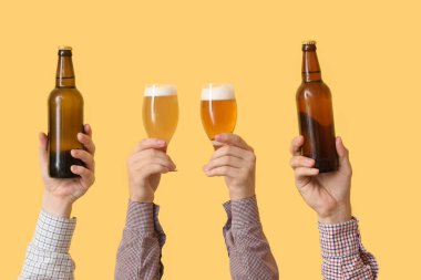 Sarı arka planda şişeli eller ve bira bardakları