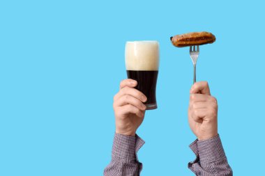 Mavi arka planda bir bardak bira ve sosisli eller.