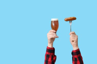 Mavi arka planda bir bardak bira ve sosisli eller.