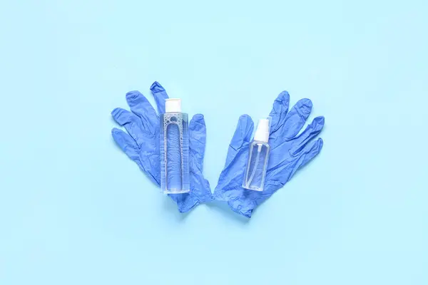 stock image Rubber gloves with bottles of different sanitizers on blue background