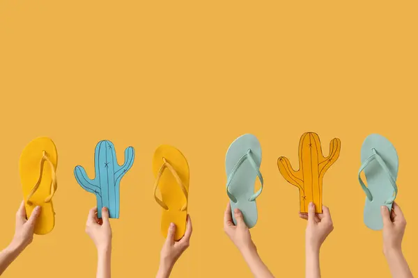 stock image Hands holding two pairs of flip flops and paper cacti on yellow background