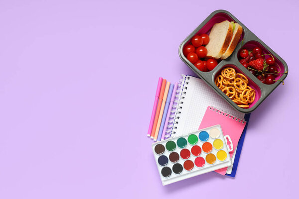 Lunch box with tasty food and school supplies on lilac background. Top view