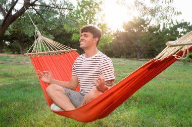 Genç adam dışarıda hamakta meditasyon yapıyor.