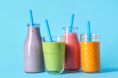 Mavi arka planda farklı taze meyve suyu kadehleri ve şişeleri.