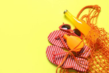 Şık çizgili parmak arası terlik, bir şişe kokteyl, güneş gözlüğü ve sarı arka planda güneş kremi.