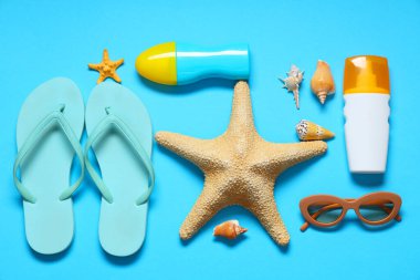 Şık çizgili terlikler, deniz kabukları, güneş gözlükleri, denizyıldızı ve mavi arka planda güneş kremi şişeleri.