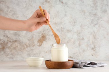 Tahta kaşıklı kadın eli ve beyaz arka planda bir kavanoz lezzetli yoğurt.