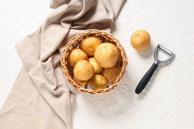 Beyaz arka planda çiğ patatesli ve soyuculu hasır kase.