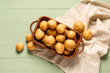 Yeşil ahşap arka planda çiğ patatesli hasır sepet