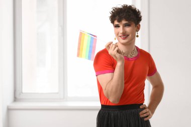 Evinin penceresinin yanında LGBT bayrağı taşıyan genç bir transseksüel kadın.