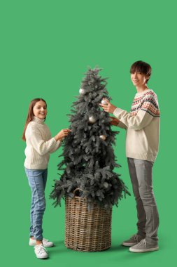 Şirin kız ve kardeşi yeşil arka planda Noel ağacı süslemişler.