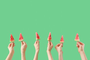 Yeşil arka planda çubuklarda karpuz dilimleri tutan kadın eller.