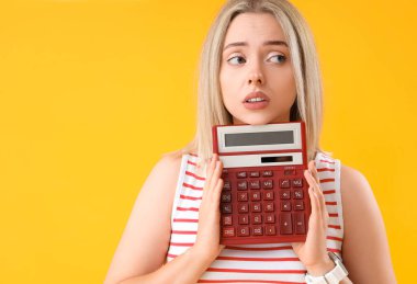 Sarı arka planda hesap makinesi olan düşünceli genç ve güzel bir kadın.