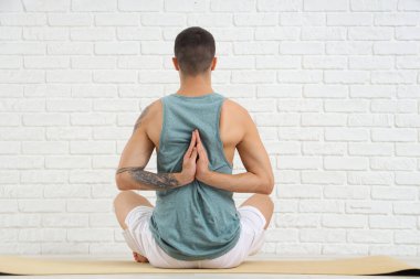 Beyaz tuğla duvarın yanında yoga yapan genç bir adam.