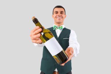 Gri arka planda şarap şişesi olan genç bir barmen.