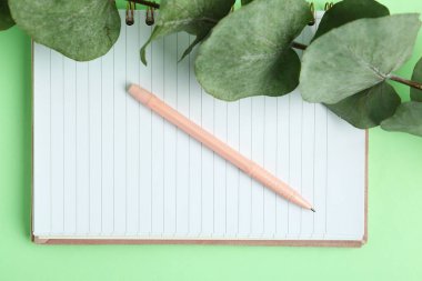 Yeşil arkaplan üzerinde not defteri ve yaprakları olan kalem
